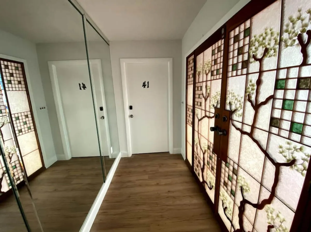 This image features stained glass doors, a mirrored wall, and numbered doors, all illuminated by warm wooden flooring. The scene is inviting and highlights architectural detailing that adds character and a sense of arrival to the home.